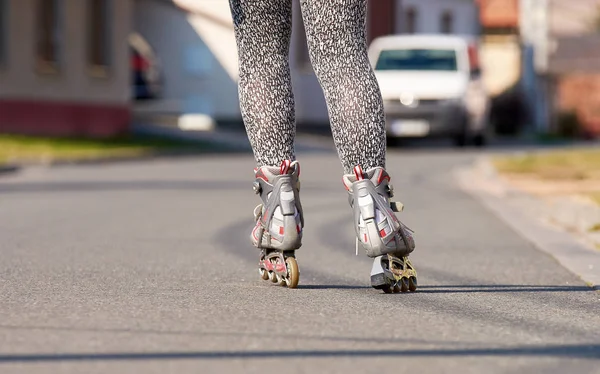 Sıralı paten ile kadın bacaklar. Otomobil ve binalar ile şehirde asfalt yol.
