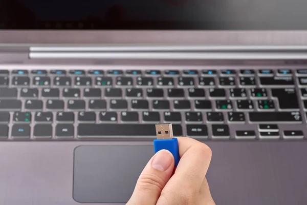 Крупный план женской руки с голубым носителем памяти USB Flash или диском. Серебряный ноутбук с клавиатурой на заднем плане — стоковое фото