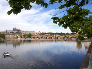 Prag'da köprü, tekne ve bulutlu mavi gökyüzü ile Vltava nehri dolgu görünümü.