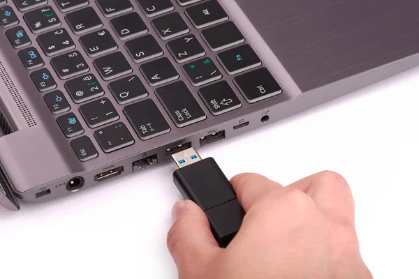 The hand of a young woman connects a USB flash drive to a port in a silver laptop with a black keyboard. Isolated on white background. — Stock Photo, Image