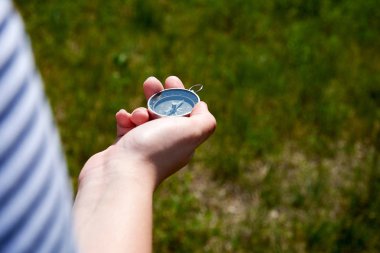 Elinde manyetik bir pusula tutan ve yolu arayan genç bir kadın. Çim arka plan ile odak çim Out.