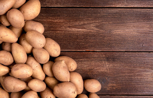 Harvested pile of potatoes on old wooden board table. Food or vegetables for cooking with space for text.