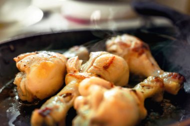 siyah bir tavada yağ ile dört kızartılmış tavuk budu 