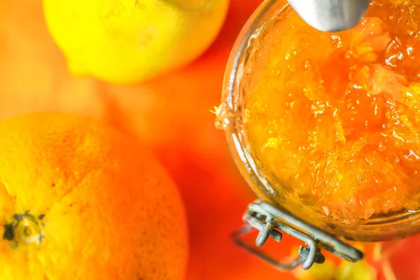 橙色果酱在一个玻璃罐子旁边的橙色和柠檬在一个橙色背景特写镜头 — 图库照片