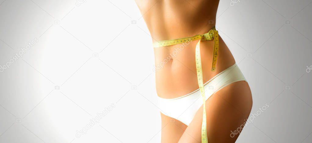 Slim european woman's body with measuring tape on the waist, isolated on the white and gray background. horizontal view with copy-space