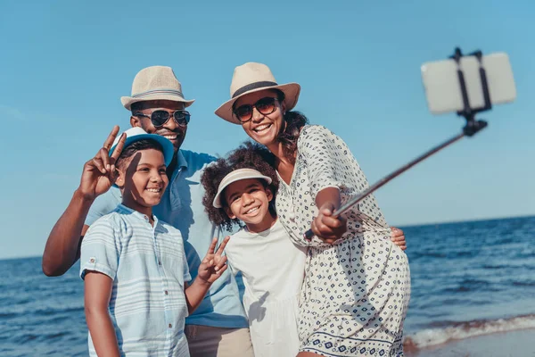 Young happy african american family taking selfie with smartphone on beach on sunny day — Stock Photo