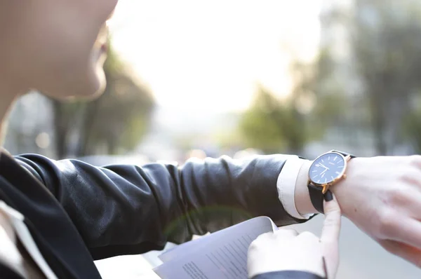 girl looks at the clock, the sun is shining in the camera