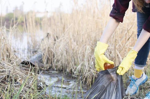 girl cleans up trash, throws a plastic bottle in the trash bag