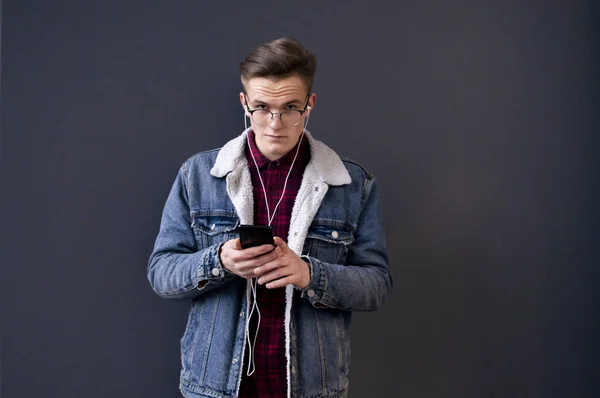 Jeune homme élégant en lunettes veste en denim et chemise écoute de la musique et regarde dans la caméra — Photo