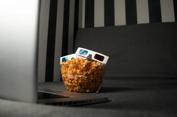 Gafas 3D, palomitas de maíz y un ordenador portátil se encuentran en el sofá de la habitación por la noche — Foto de Stock