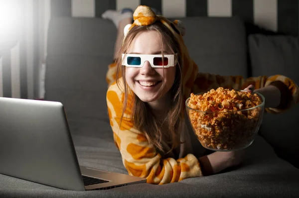 Jovencita viendo una película en casa en pijama con gafas 3d, comiendo palomitas de maíz y sentada en el sofá de la habitación — Foto de Stock