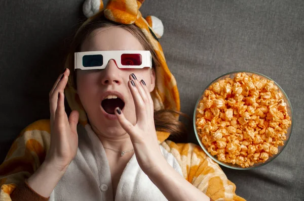 Junges süßes Mädchen liegt auf grauem Hintergrund in 3D-Brille isst Popcorn und schaut sich einen Film an — Stockfoto