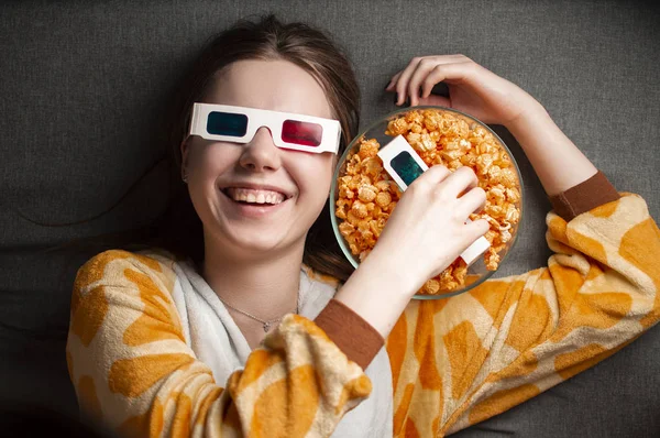 Junges süßes Mädchen liegt auf grauem Hintergrund in 3D-Brille isst Popcorn und schaut sich einen Film an — Stockfoto