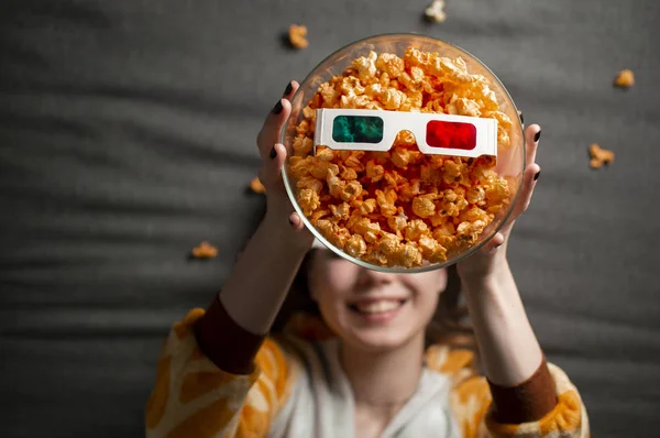 Hermosa chica en pijama come palomitas de maíz, se encuentra en un fondo gris en gafas 3d y mira una película — Foto de Stock
