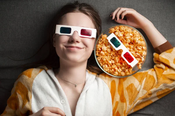 Молода мила дівчина лежить на сірому фоні в 3d окулярах їсть попкорн і дивиться фільм — стокове фото