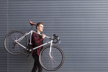 young handsome guy carries a broken bike on his shoulders against the wall, the student goes on foot