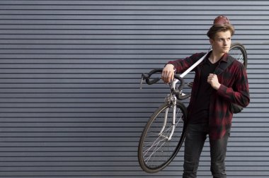 young handsome guy carries a broken bike on his shoulders against the wall, the student goes on foot