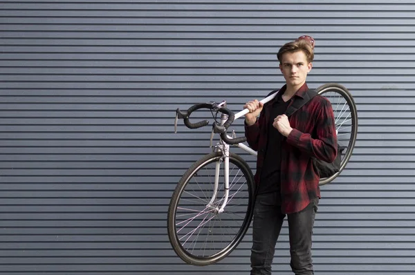 Молодой красивый парень несет сломанный велосипед на плечах к стене, студент идет пешком — стоковое фото