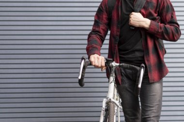 adam elinde bir bisiklet tutar ve çizgili bir duvara karşı duruyor, bir sırt çantası ile öğrenci toplandı ve hazır