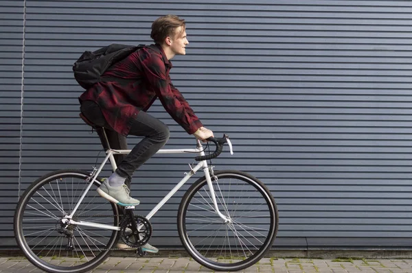 young stylish guy rides a white bicycle on a gray striped wall, student travels to school