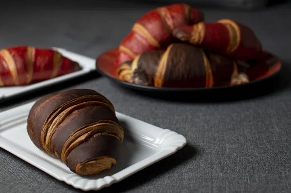 Шоколадные и красные круассаны лежат на тарелках на серой ткани, булочки крупным планом — стоковое фото