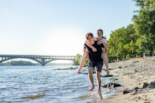 mutlu adam ve kız deniz kenarında yalınayak koşmak, neşeli çift deniz ve gökyüzü nün arka planına karşı şehir dışında yürüyor