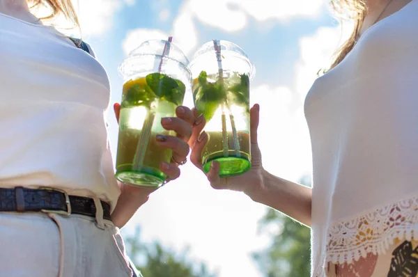 女の子はモヒートでプラスチック製のメガネを立って保持し、彼らは飲み物でメガネをクリンクし、さわやかな飲み物のクローズアップ — ストック写真