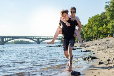 mutlu adam ve kız deniz kenarında yalınayak koşmak, neşeli çift deniz ve gökyüzü nün arka planına karşı şehir dışında yürüyor