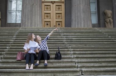 iki çekici öğrenci üniversite dışında oturup okulun arka planı hakkında ders aldıklarını söylüyorlar.
