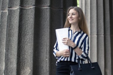 güzel öğrenci üniversite nin yanında duran, elinde kağıtları tutarak ve üniversitenin arka planına karşı gülümseyerek, o okula gider