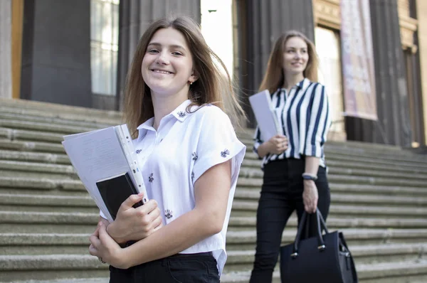 Δύο όμορφα φοιτητές στέκονται κοντά στο Πανεπιστήμιο, κρατώντας χαρτιά στα χέρια τους και χαμογελώντας στο φόντο του κολλεγίου, πηγαίνουν στο σχολείο — Φωτογραφία Αρχείου