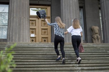 kız öğrenciler okula giderler, üst kata çıkarlar, el ele tutuşmuşlar, kız arkadaşları derslere koşarlar.