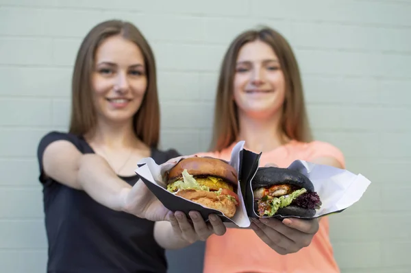 젊은 아름다운 여자 학생들은 푸른 벽 근처에 서서 햄버거와 미소를 잡고, 그들은 패스트 푸드를 먹을 때 행복 — 스톡 사진