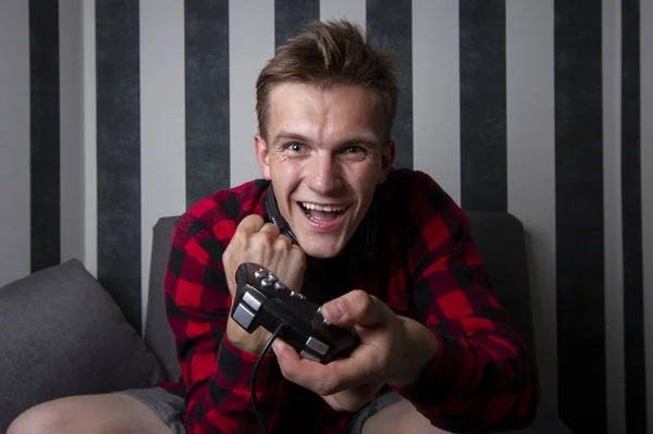 Cara joga videogames em casa no computador à noite, ele segura joysticks e está focado no jogo, o adolescente joga o console — Fotografia de Stock