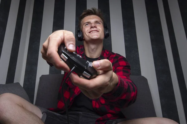 Cara joga videogames em casa no computador à noite, ele segura joysticks e está focado no jogo, o adolescente joga o console — Fotografia de Stock