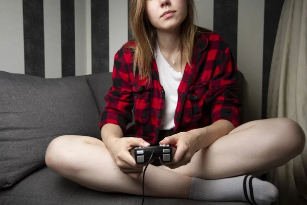 Niña juega en la consola, se sienta en casa en el sofá y sostiene el joystick, primer plano del dispositivo —  Fotos de Stock
