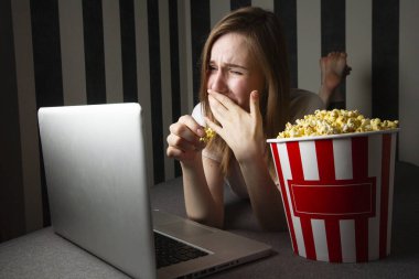 bir dizüstü bilgisayar da gece bir Tv programı izlerken ve patlamış mısır yemek genç bir kız, o kanepede yatarken bir bilgisayar kullanır