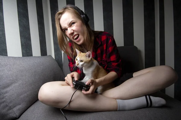 Menina agressiva senta-se no sofá e joga jogos de vídeo no joystick, ela grita e perde no console — Fotografia de Stock