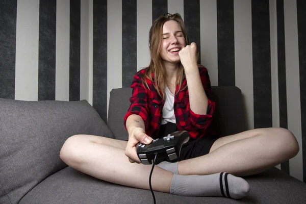 Młoda dziewczyna siedzi na kanapie i gra w gry wideo, trzyma joystick i wygrywa na konsoli — Zdjęcie stockowe