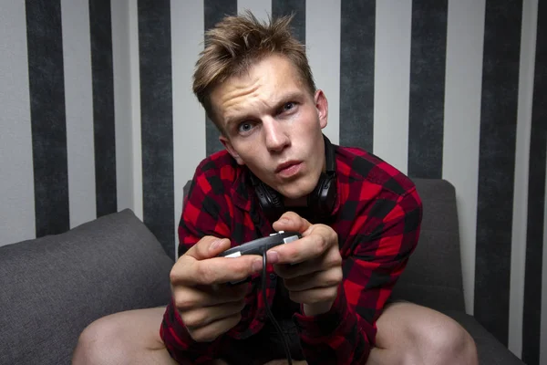 Jovem cara joga jogos de vídeo no console, ele se senta em casa no sofá e segura o joystick à noite — Fotografia de Stock