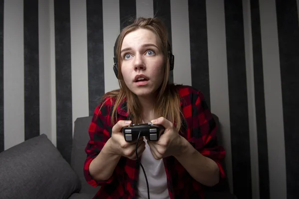 Jovem menina senta-se no sofá e joga o console no joystick, ela está focada em jogos de vídeo — Fotografia de Stock