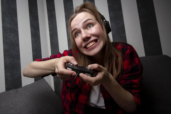 Jovem menina senta-se no sofá e joga videogames, ela segura o joystick e ganha no console — Fotografia de Stock