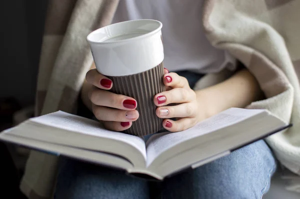 Jeune fille est assise près de la fenêtre, couverte d'une couverture, elle lit un livre et boit du thé, gros plan — Photo
