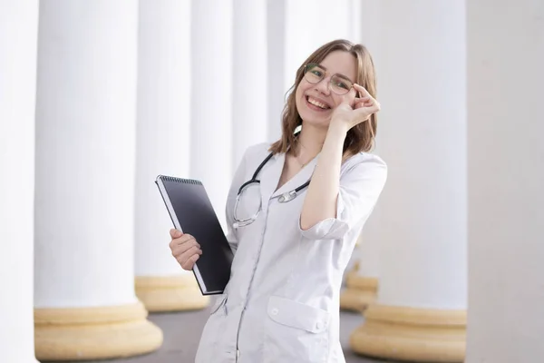 young girl student at a medical university standing in the corridor, portrait of an attractive nurse near the hospital, happy female doctor with a stethoscope in uniform