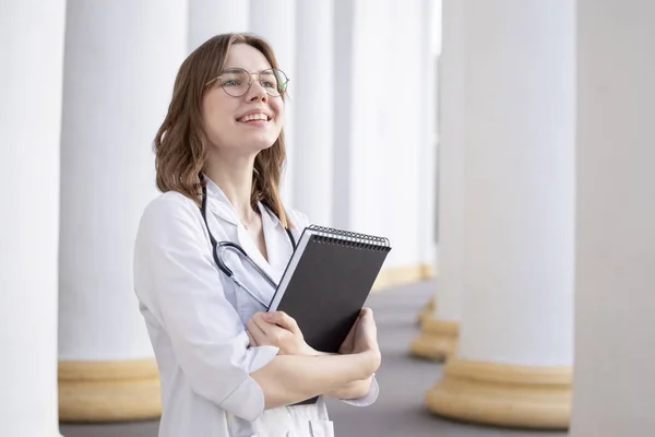 young girl student at a medical university standing in the corridor, portrait of an attractive nurse near the hospital, happy female doctor with a stethoscope in uniform