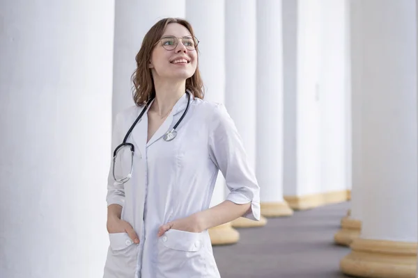 young girl student at a medical university standing in the corridor, portrait of an attractive nurse near the hospital, happy female doctor with a stethoscope in uniform