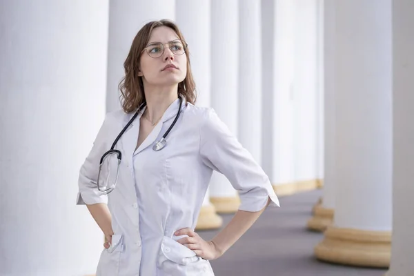 young girl student at a medical university standing in the corridor, portrait of an attractive nurse near the hospital, happy female doctor with a phonendoscope in uniform
