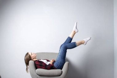 genç kız bacakları yukarı kaldırdı beyaz bir duvara karşı yumuşak rahat bir sandalyede oturuyor, bir hipster öğrenci dinlenme ve hayal, kopya alanı