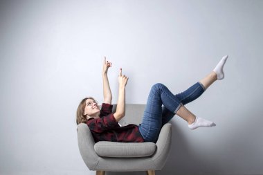 genç kız bacakları yukarı kaldırdı beyaz bir duvara karşı yumuşak rahat bir sandalyede oturuyor, bir hipster öğrenci dinlenme ve hayal, kopya alanı