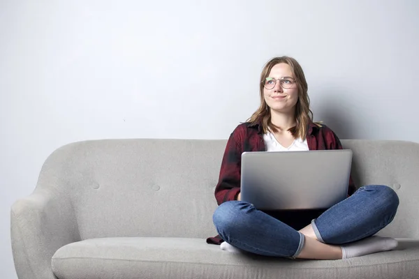 ソファに座ってコーヒーを飲むノートパソコンを持つ若い女の子、白い空白の壁に対してコンピュータを使用している女性、彼女はフリーランスと夢を見て、スペースをコピー — ストック写真